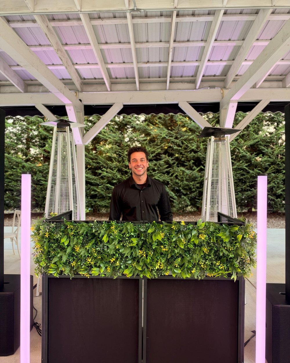 Lucas Morais smiling behind his DJ booth with light tubes at an outdoor wedding venue